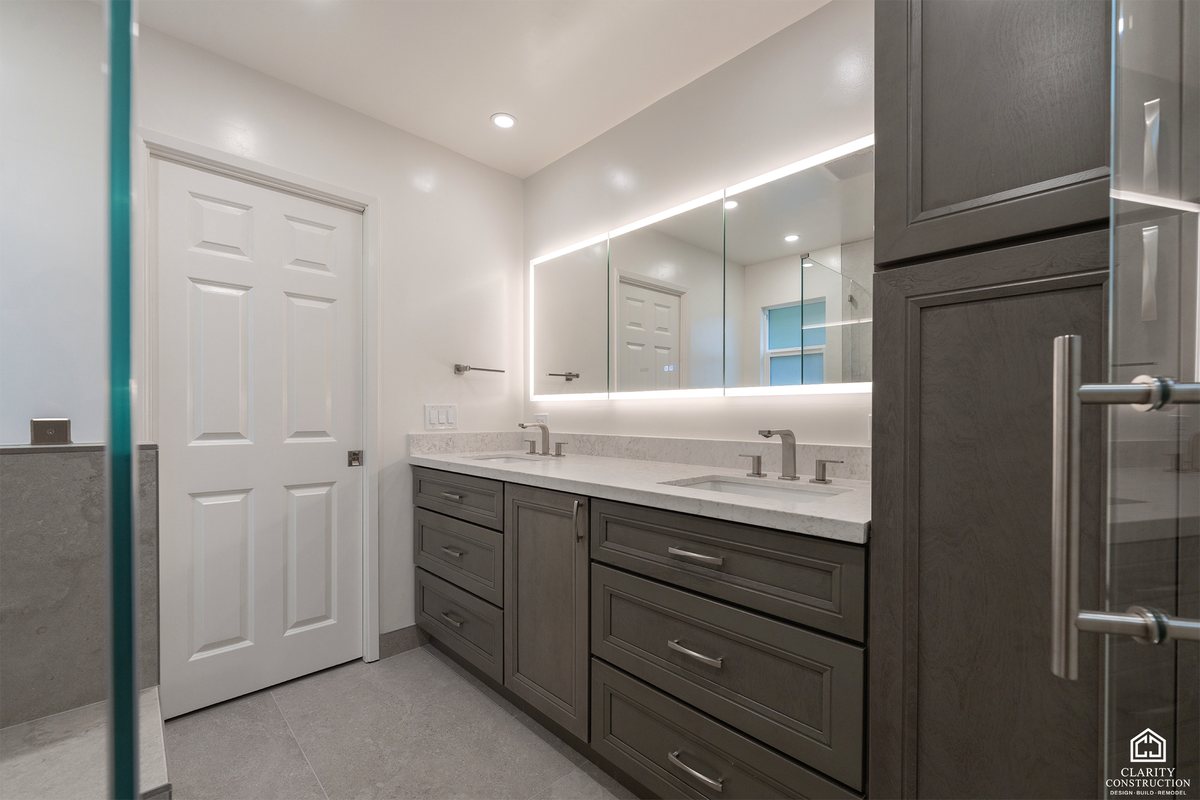 Remodeled family bathroom with a gray double vanity, backlit mirror and a full height linen cupboard