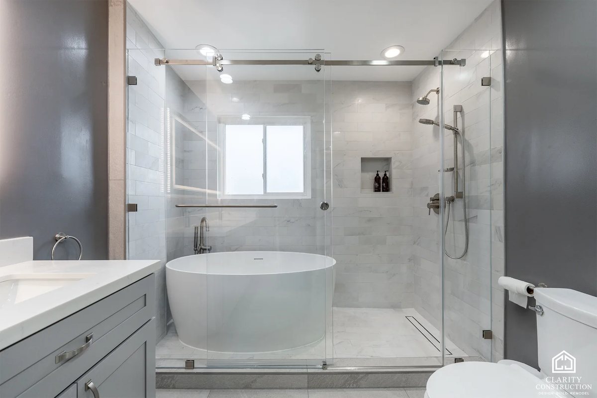 Primary bathroom with a freestanding tub and shower behind sliding glass and a gray double vanity