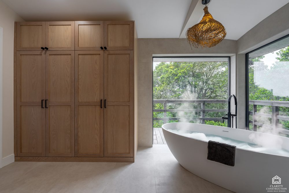 Full height white oak cabinetry beside a freestanding tub under a woven pendant