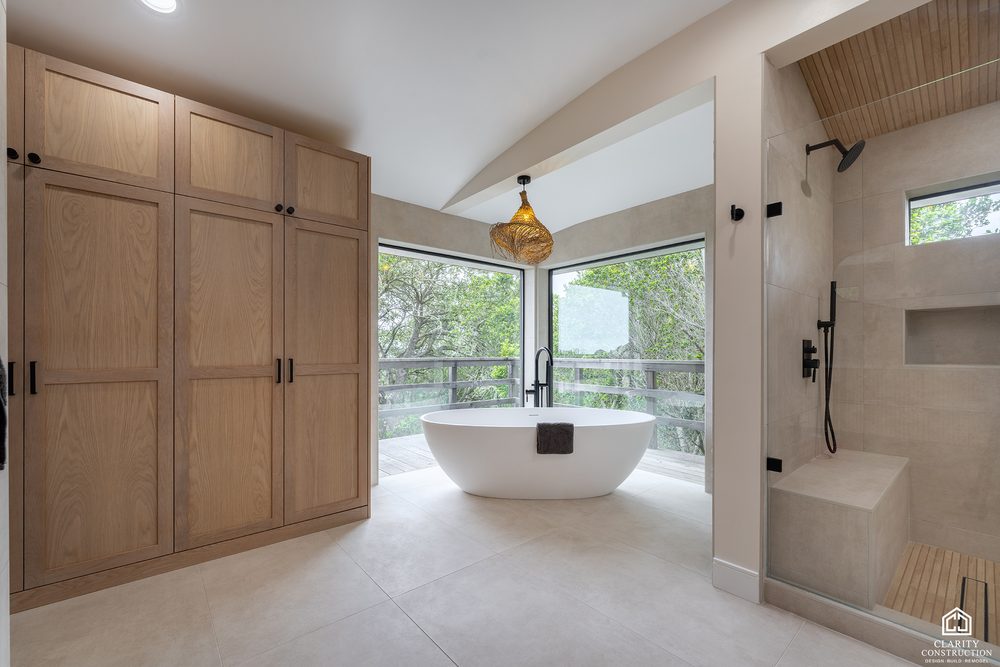 White oak wardrobe wall facing a freestanding tub and a tiled walk in shower