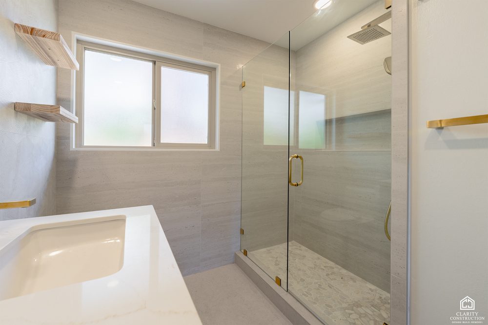 Walk in shower in large format stone tile with brass fittings and floating oak shelves
