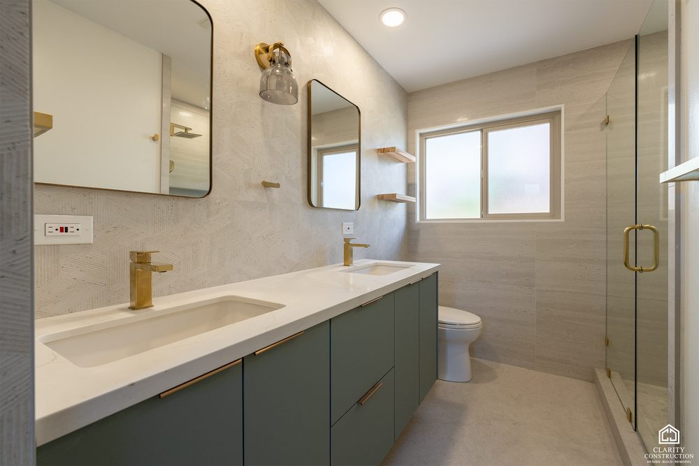 Sage green double vanity with brass faucets, arched mirrors and a glass shower