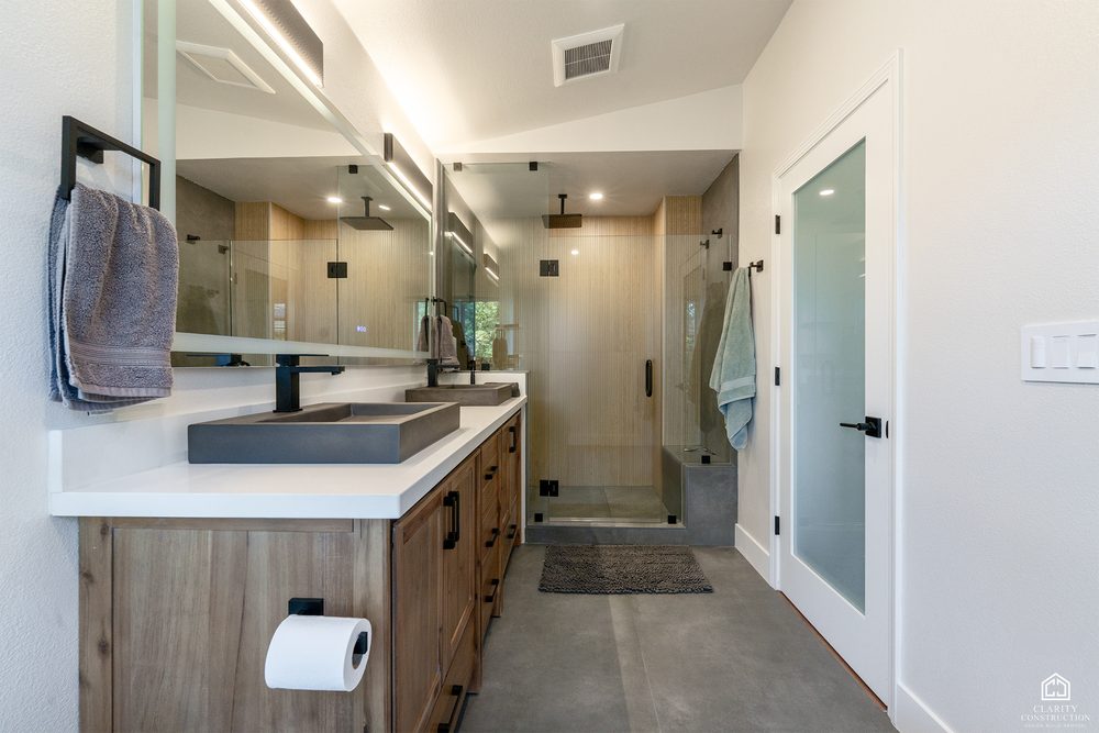 Long bathroom with a walnut vanity, black stone basin and a glass shower at the far end