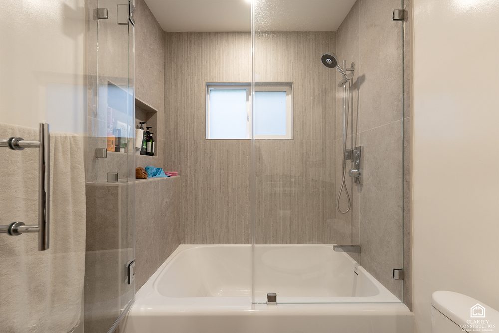 Tub shower with a sliding glass screen, tiled niche and a wall mounted hand shower