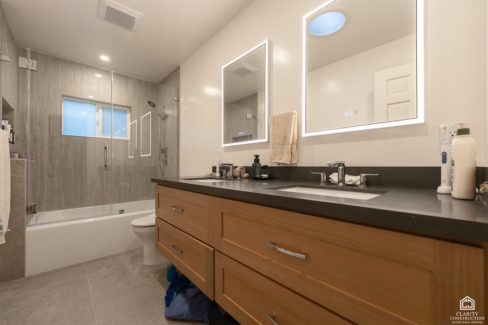 Remodeled bathroom with an oak double vanity, backlit mirror and a tub under the window