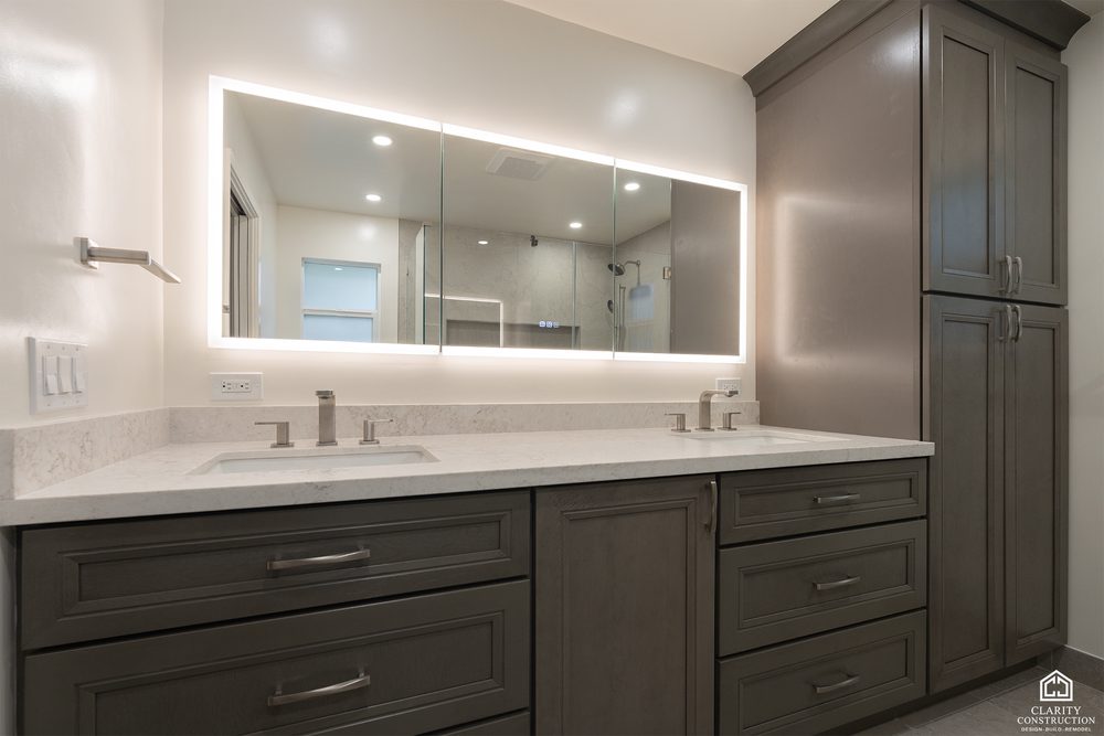 Gray shaker double vanity with a full width backlit mirror and fitted storage