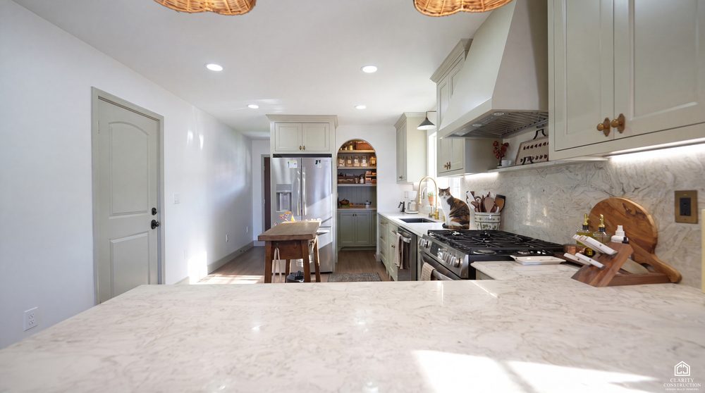 Sage green kitchen with marble counters and an arched pantry door, in an empty room
