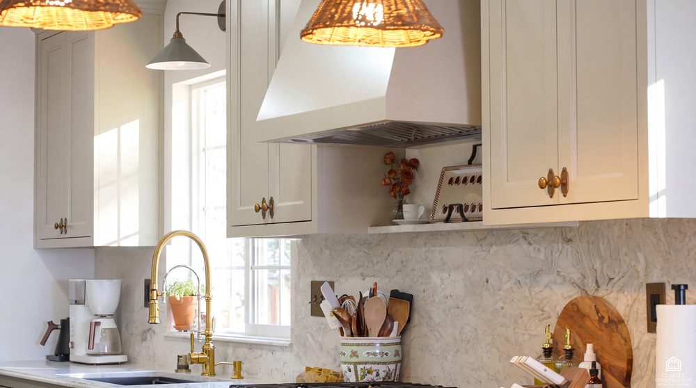 Kitchen sink under a window with a brass bridge faucet and a marble slab backsplash