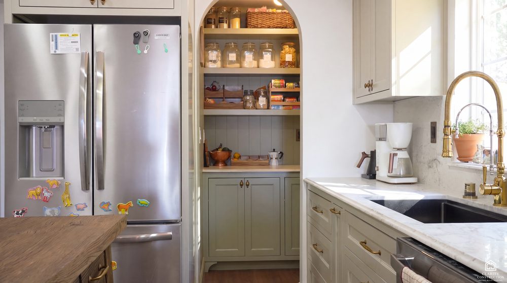 Counter depth refrigerator beside a fitted pantry with brass hardware and a marble top