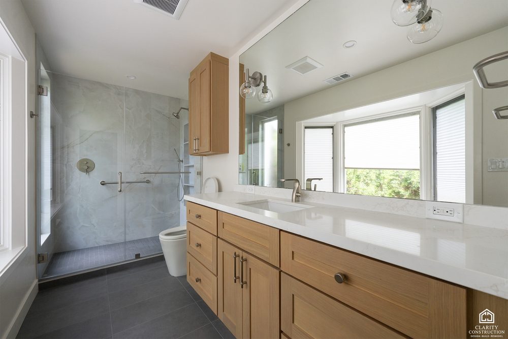 Oak double vanity with a stone top facing a walk in shower with a grab rail