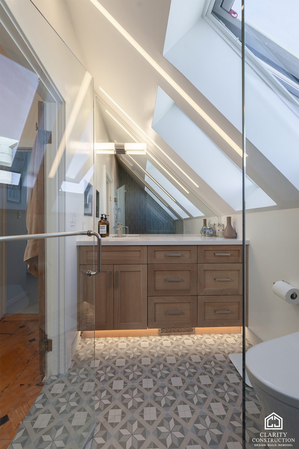 Attic bathroom with an oak vanity, patterned floor tile and a skylight above the shower