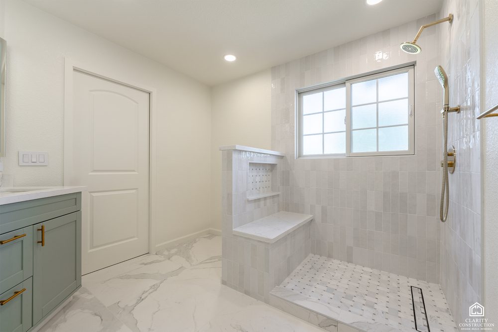 Walk in shower with a tiled bench, brass fittings and a sage green vanity opposite