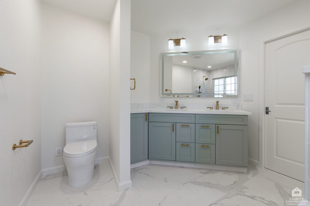 Sage green double vanity with brass faucets and a marble tiled floor