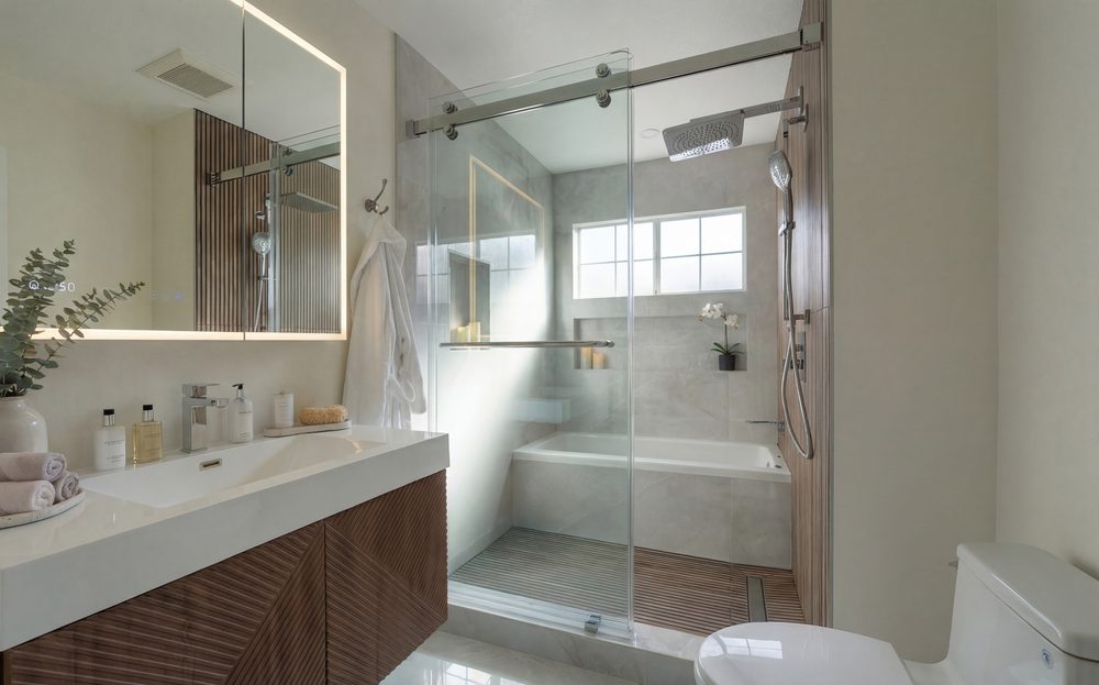 Fluted walnut vanity with a backlit mirror beside a glass shower and a tub