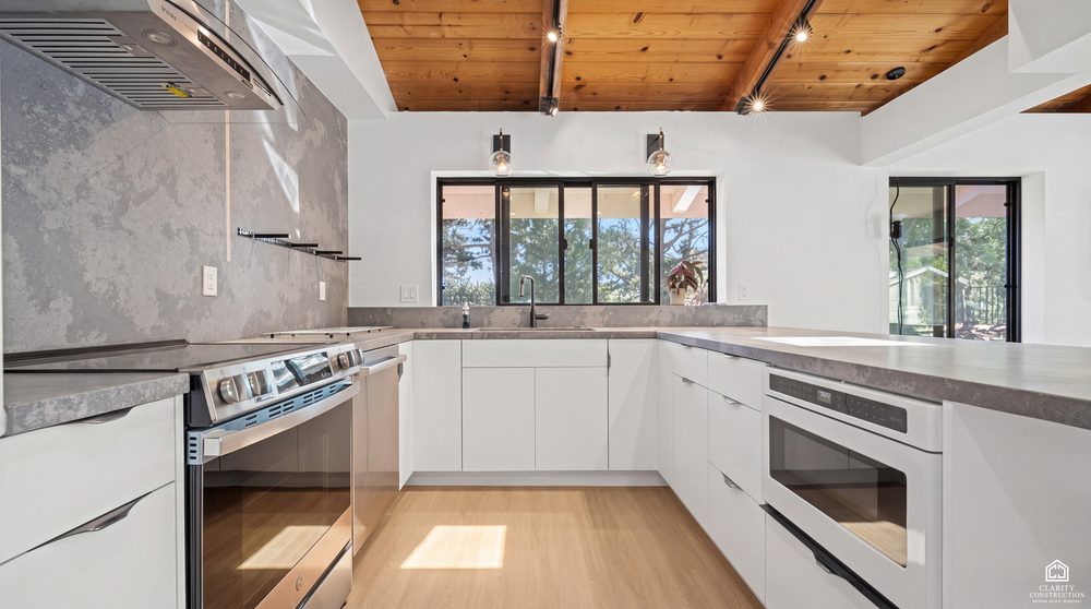 Handleless white kitchen with a stone backsplash under an open beam cedar ceiling