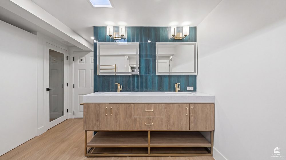 Floating oak vanity against a teal tiled wall with twin mirrors and brass faucets