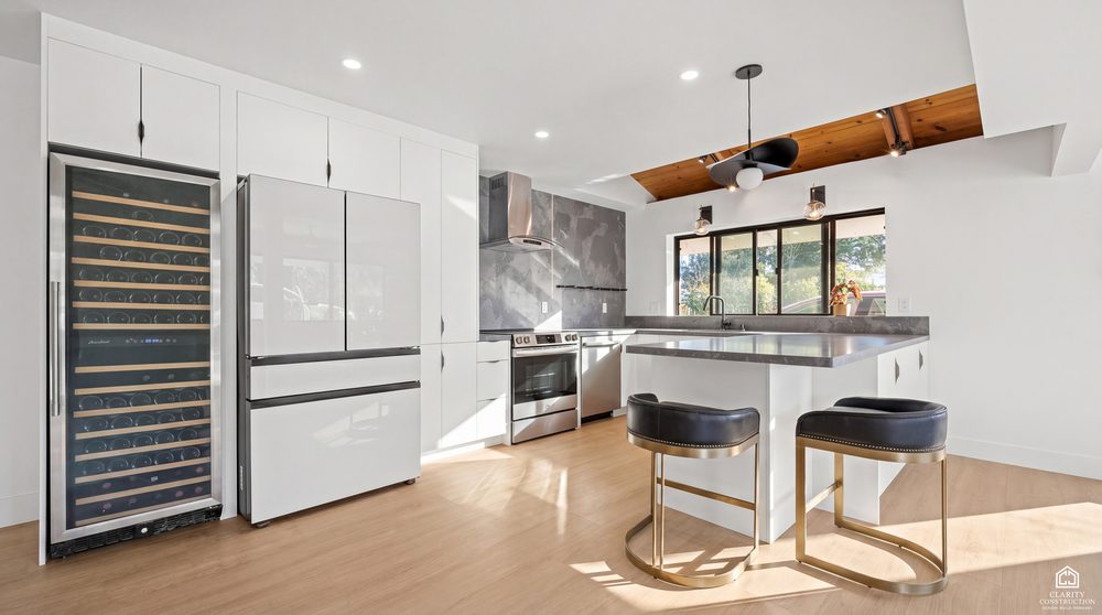Kitchen island with brass bar stools, a tall wine fridge and a cedar ceiling above