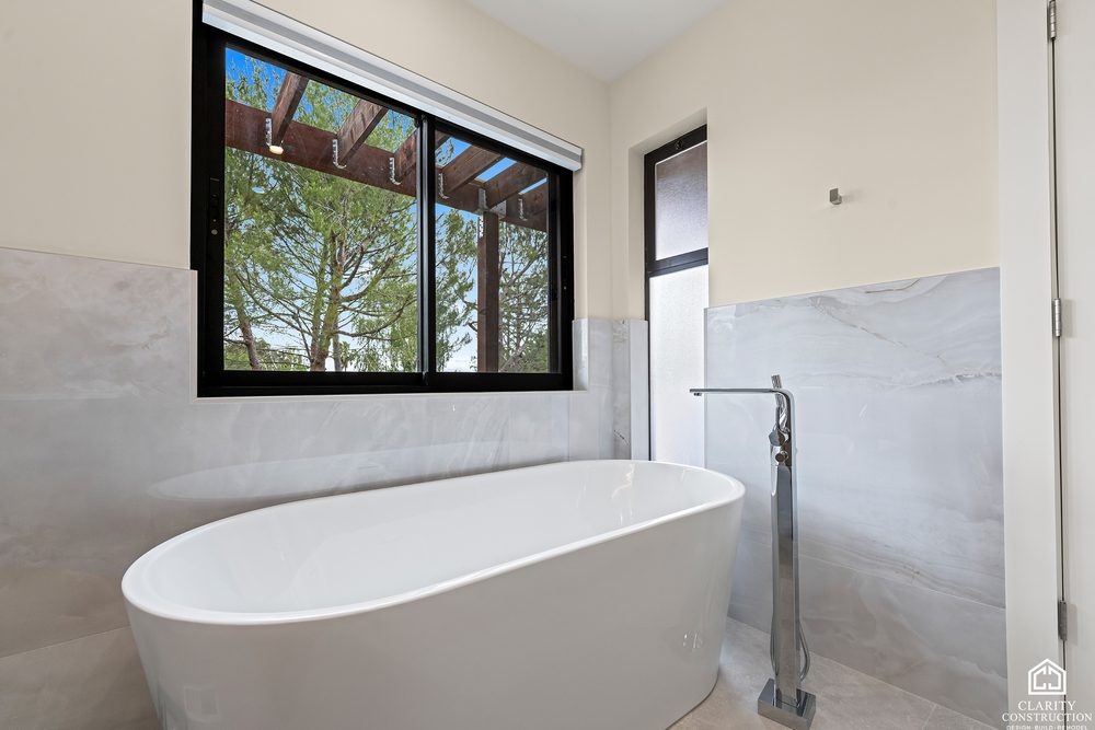 Freestanding tub under a clerestory window with marble walls and a floor mounted filler
