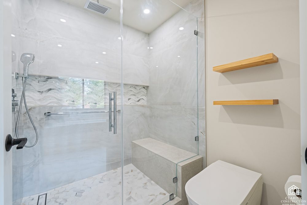 Marble walk in shower with a built in bench, floating oak shelves and a rain head