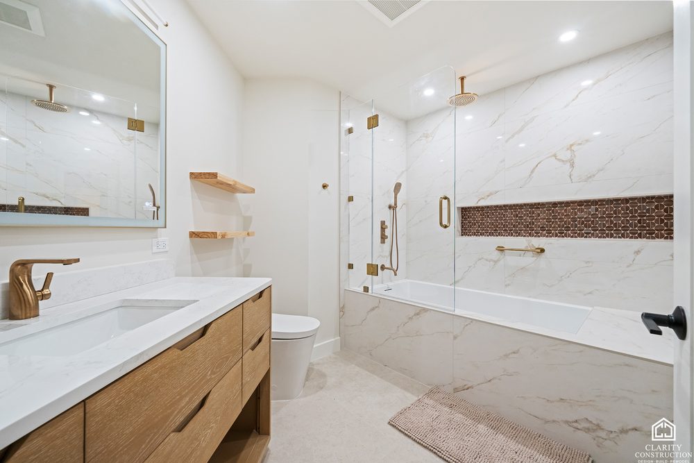 Marble bathroom with an oak vanity, brass fittings and a tub behind a glass screen