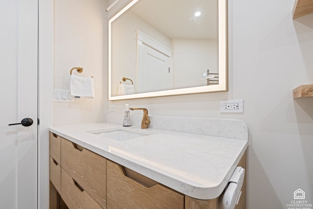 Fluted oak vanity with a stone top and a brass faucet under a lit mirror