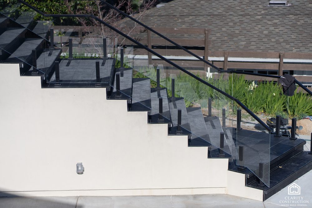 Exterior stair with a glass railing and dark steel handrail climbing to the front door