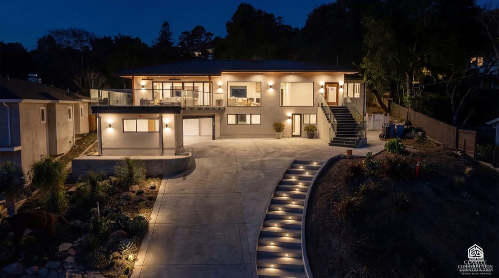 The finished house at dusk with the driveway, stepped path lights and the rooms lit inside