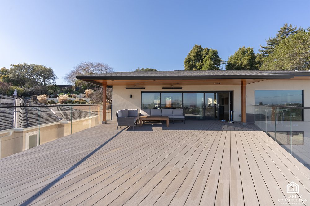 Wide composite deck with a glass railing running the length of the house