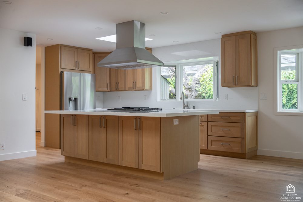 Kitchen island with a gas cooktop under a stainless chimney hood
