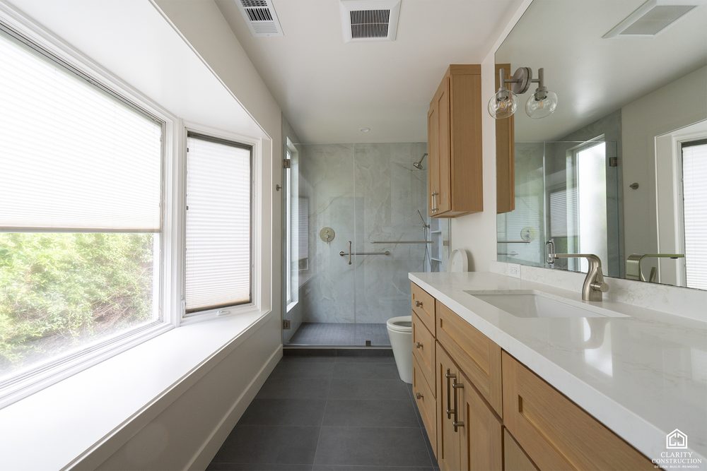 Long wood vanity with a white counter under a wide window in the primary bathroom