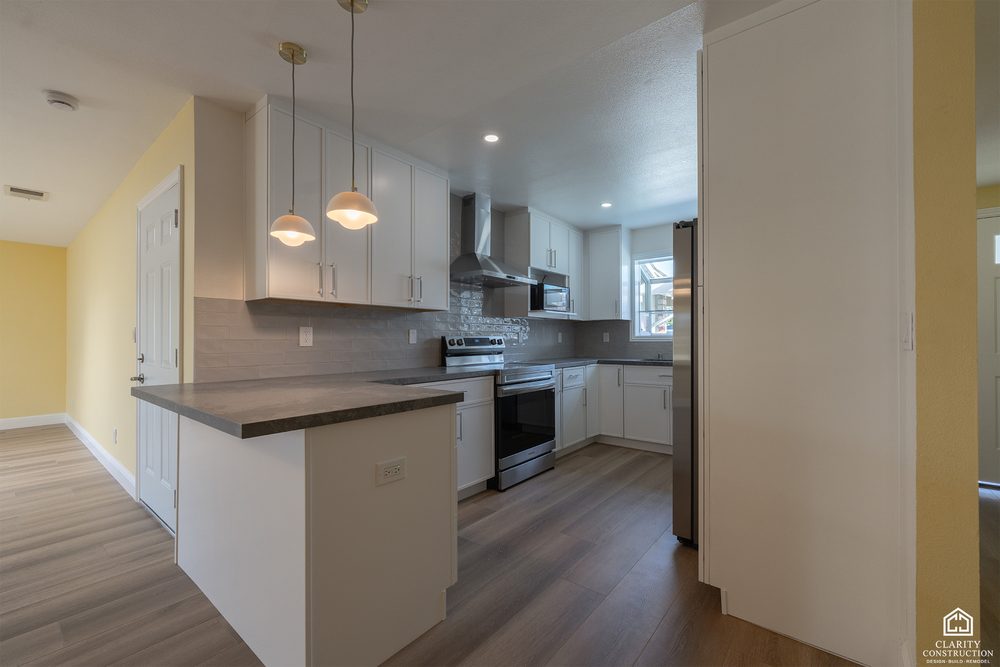 New white kitchen with dark counters and a stainless hood seen from the open living room