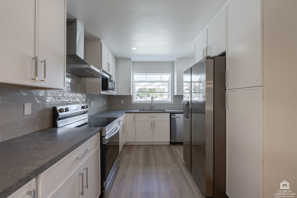 White kitchen with dark quartz counters, a stainless hood and a window over the sink
