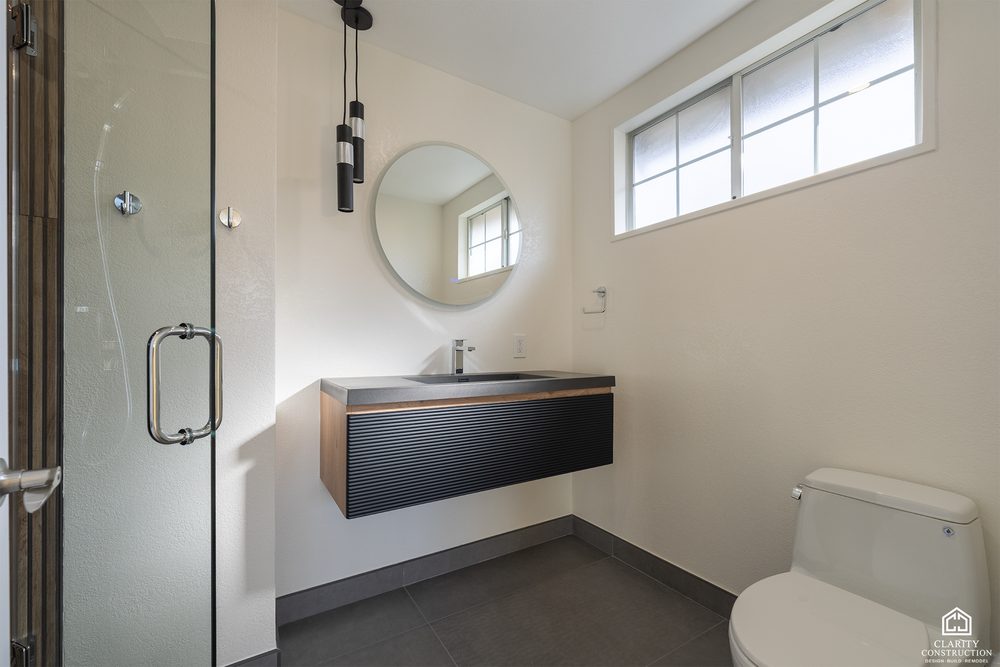 Second bathroom with a floating vanity, a round mirror and a glass shower