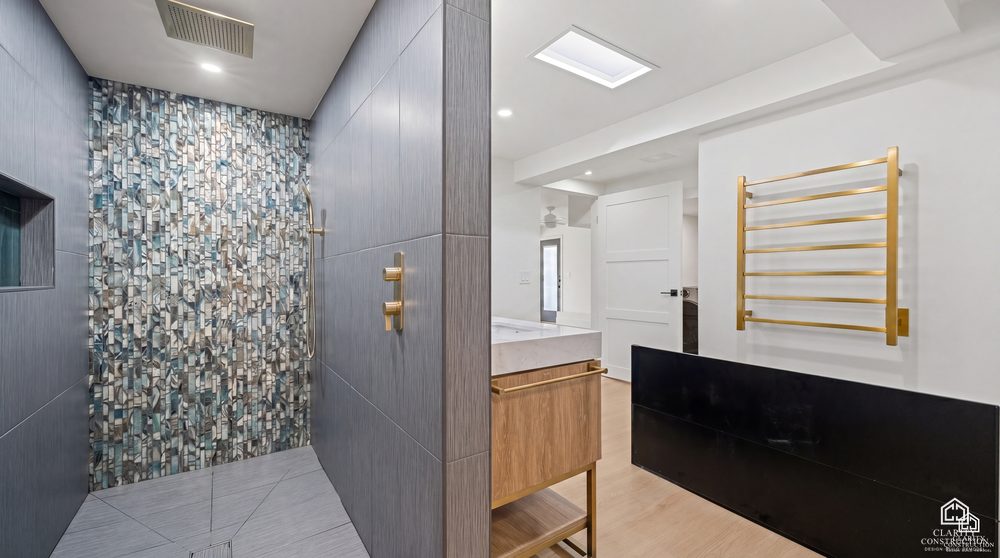 Walk-in shower with green mosaic tile and a brass towel warmer