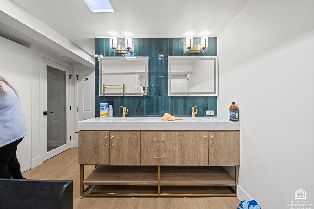 Wood vanity with two sinks and green mosaic tile behind the mirror
