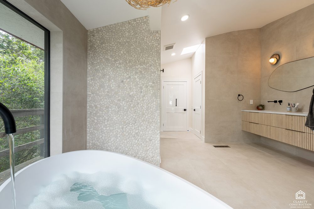 Freestanding tub against a textured pebble accent wall with the vanity beyond
