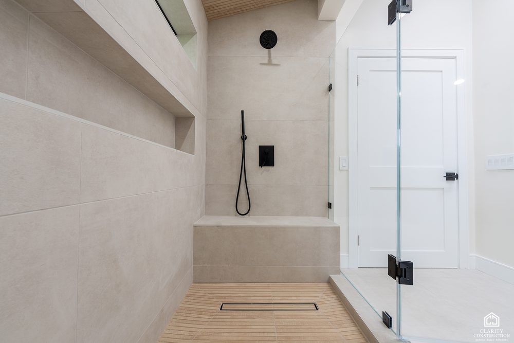 Shower with a black rain head and hand shower behind a frameless glass door