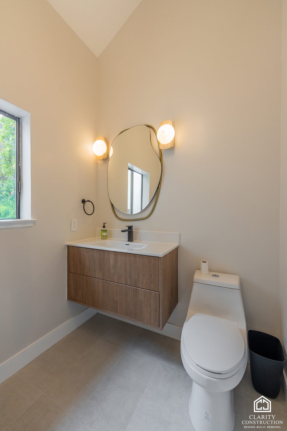 Walnut vanity with a round mirror and a wall sconce in the second bathroom
