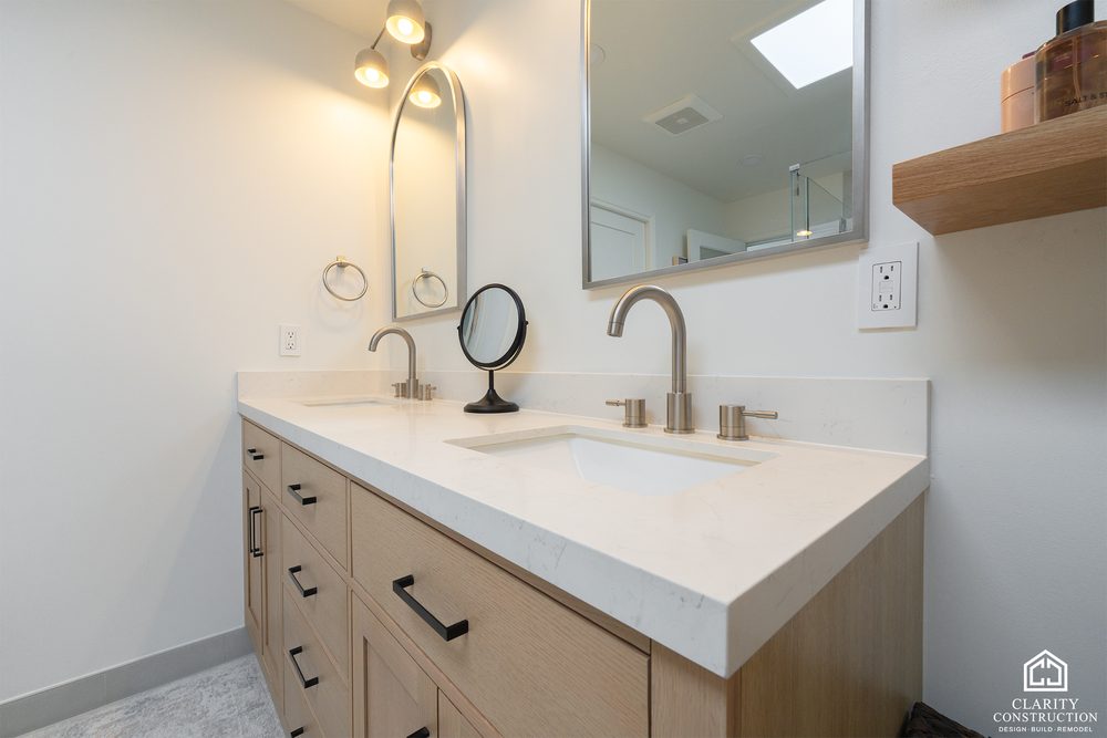 White oak vanity with a white counter, brushed nickel faucet and an arched mirror