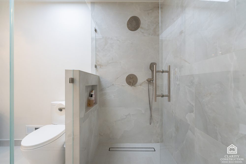 Shower with a linear drain and a half wall of stone-look tile
