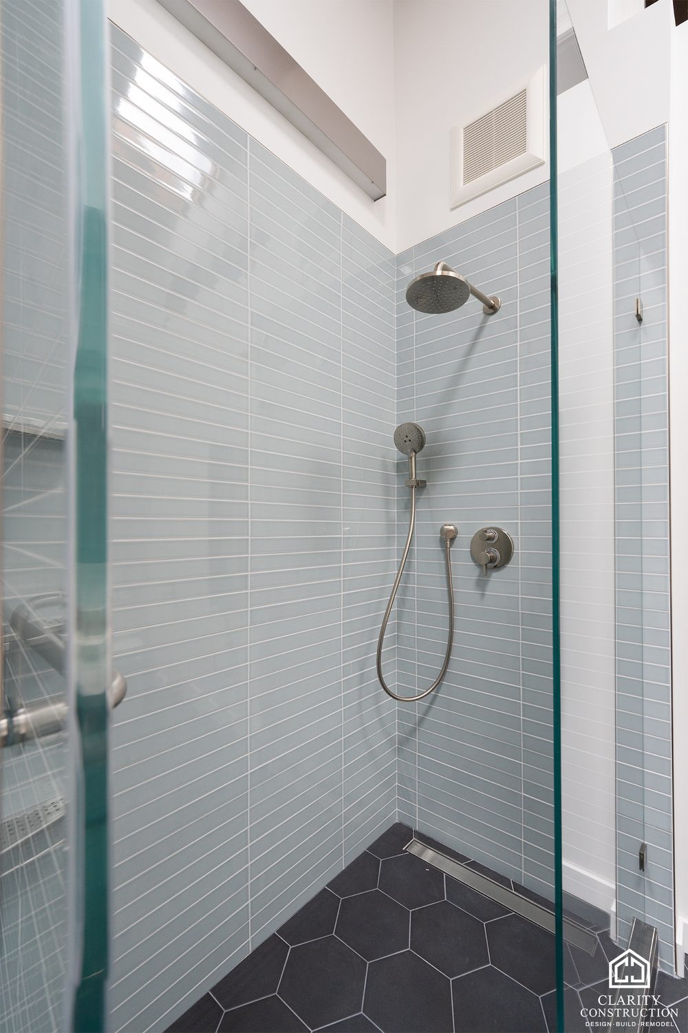 Walk-in shower lined in pale blue glass tile with a charcoal hex floor
