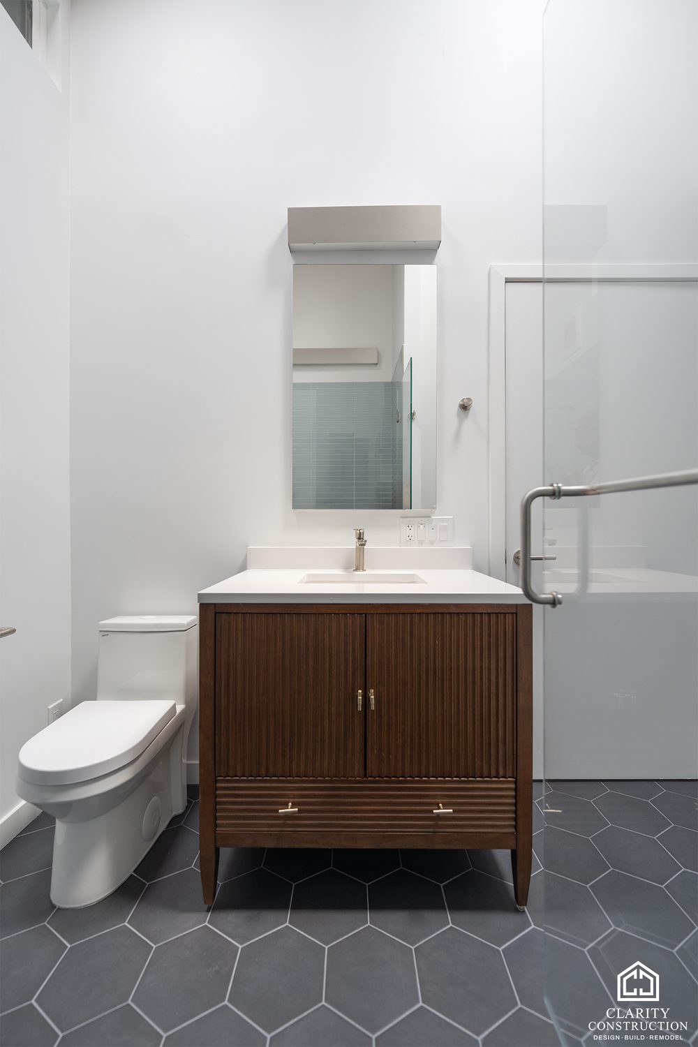 Walnut vanity with a mirror and a wall sconce beside the toilet