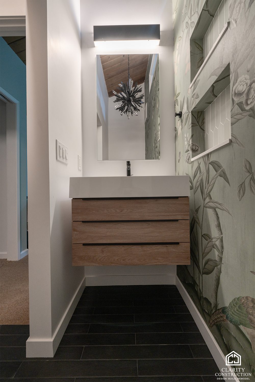 Floating oak vanity with a white sink under a mirror and floral wallpaper