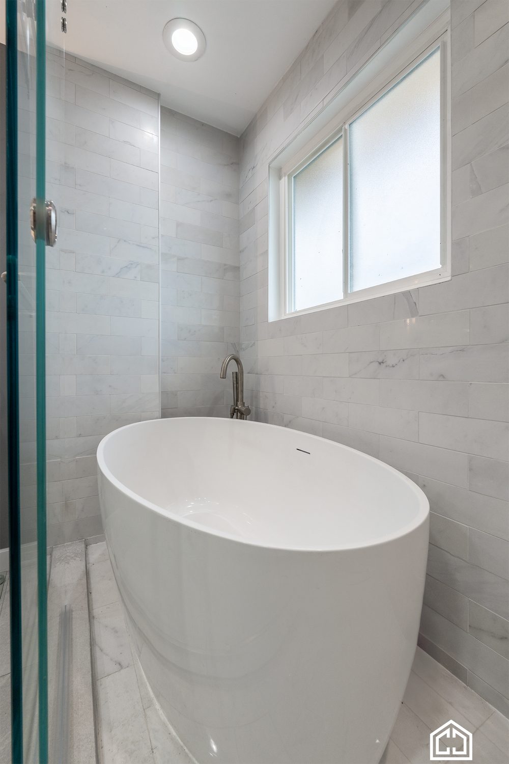 Freestanding tub under a window inside the marble-look tile wet room