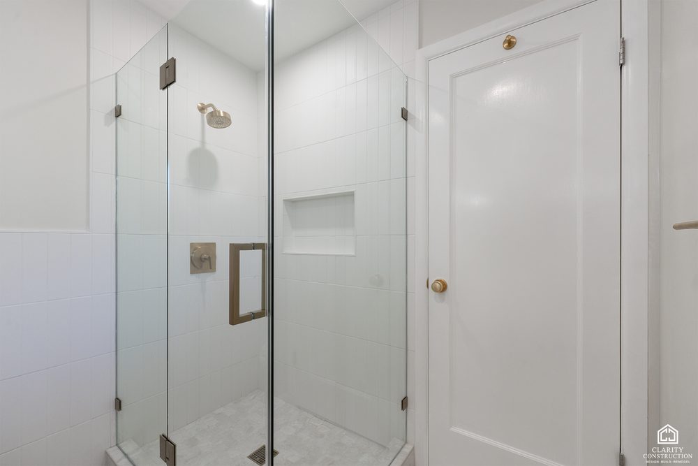 White tile walk-in shower with a brass rain head behind a frameless glass door