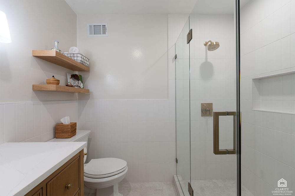 Floating oak shelves and a brass towel ring beside the glass shower