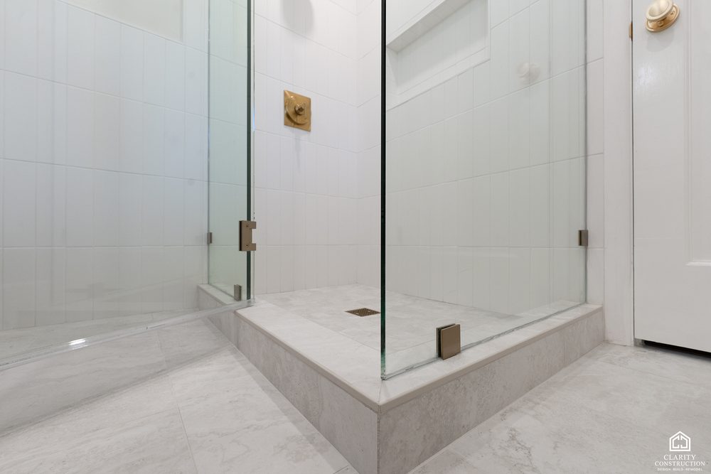 Marble-look shower curb and floor with brass hardware on the glass door