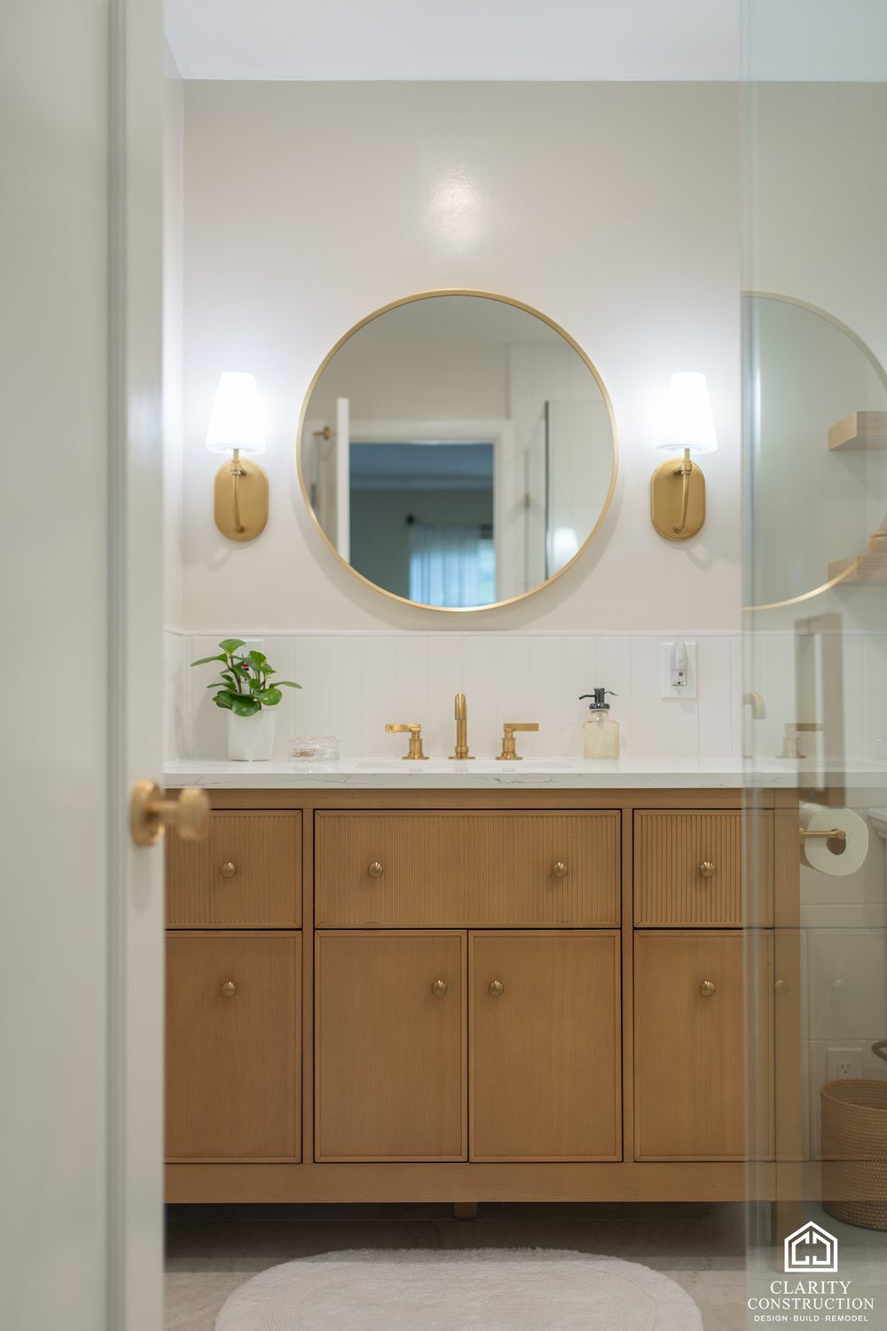 Fluted oak vanity with a round brass mirror and a plant on the counter