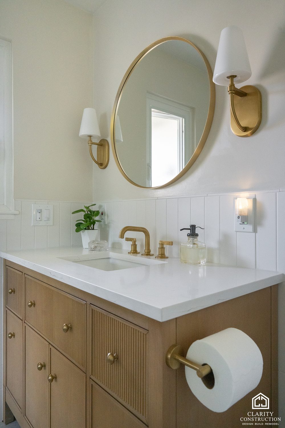 Round brass mirror and sconces over the oak vanity