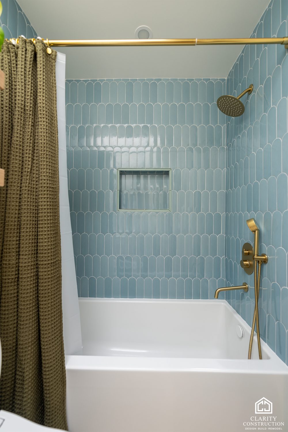 Tub with blue picket tile, a brass curtain rod and an olive shower curtain
